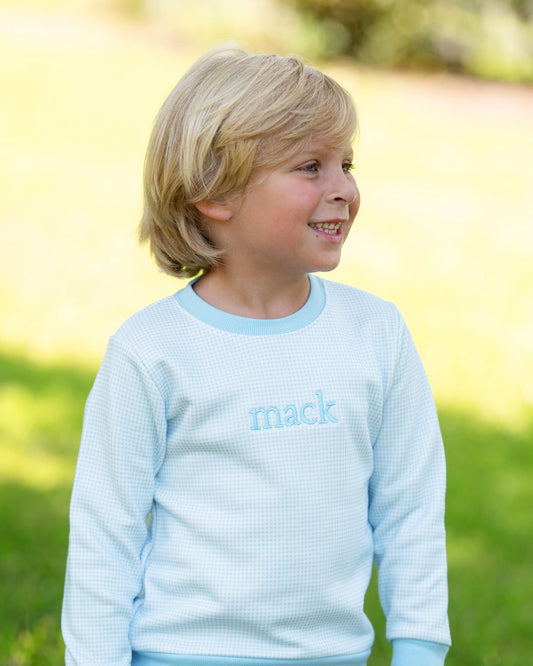 A young blonde boy wearing a light blue waffle-knit long-sleeve shirt with the name 'mack' embroidered on the chest, standing outdoors in a grassy area.