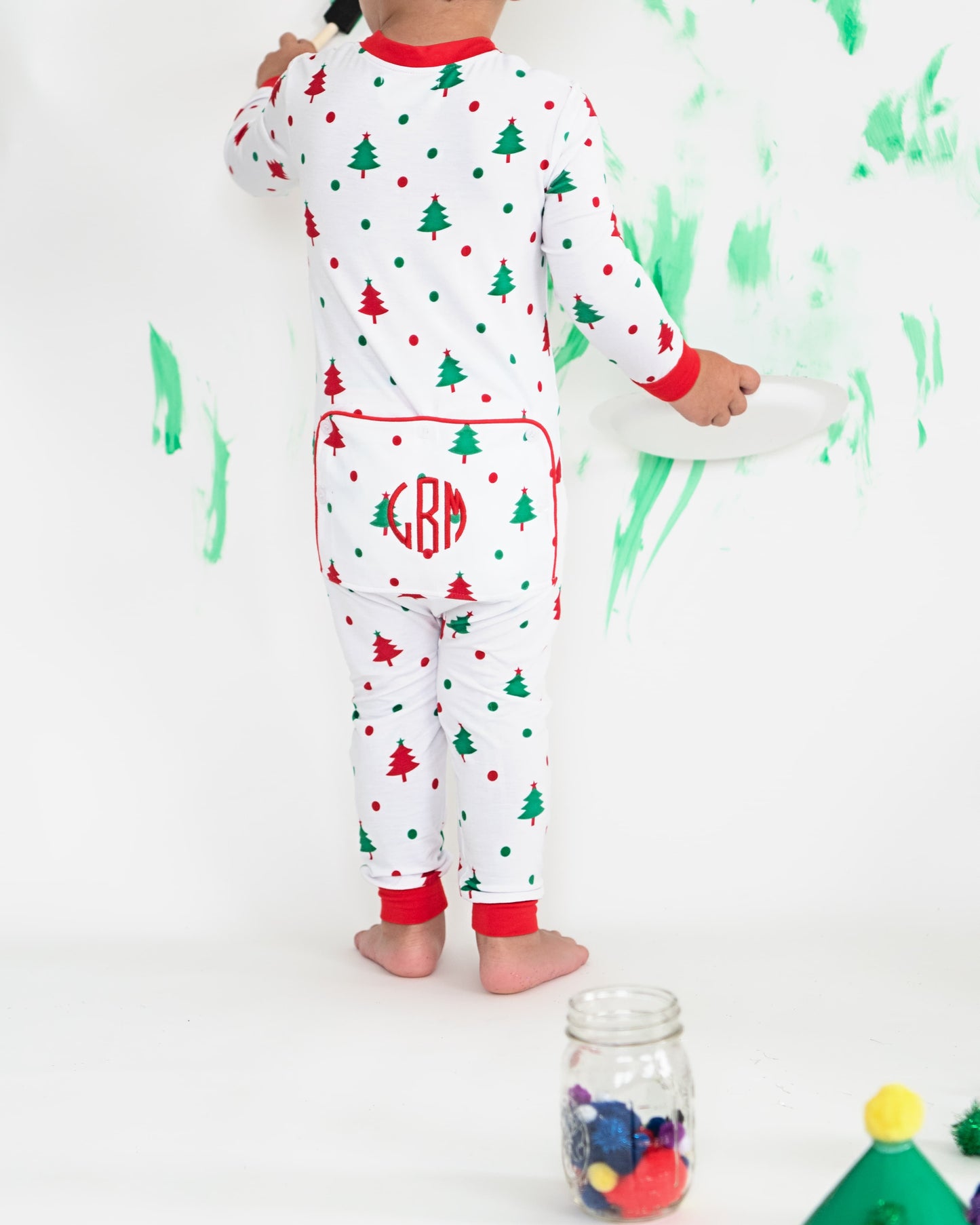 A young child wearing holiday pajamas painting on the wall. 