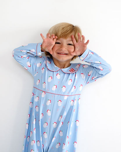 A young child with blonde hair wearing a light blue long-sleeve pajama dress with a white snowman pattern and red trim, posing with their hands around their eyes against a plain white background.