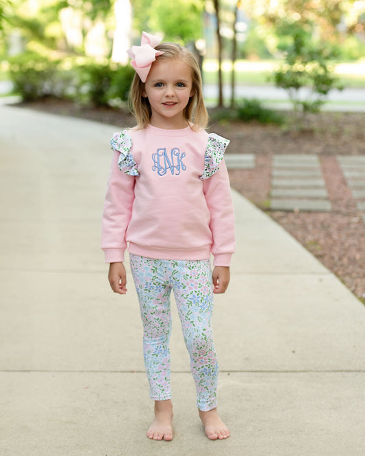A young girl standing on a sidewalk wearing floral leggings and a pink sweatshirt