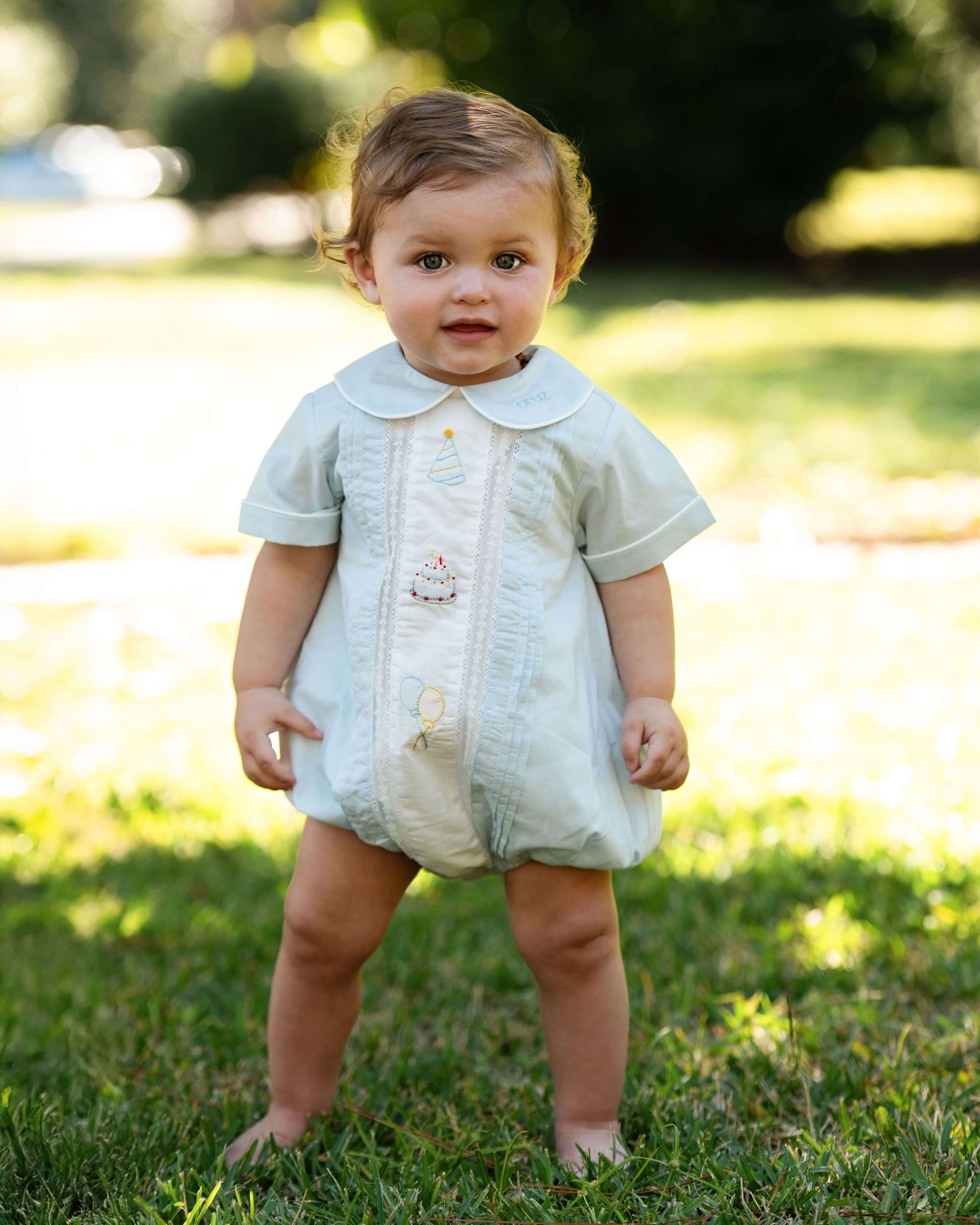 Baby in a light-colored outfit standing on grass