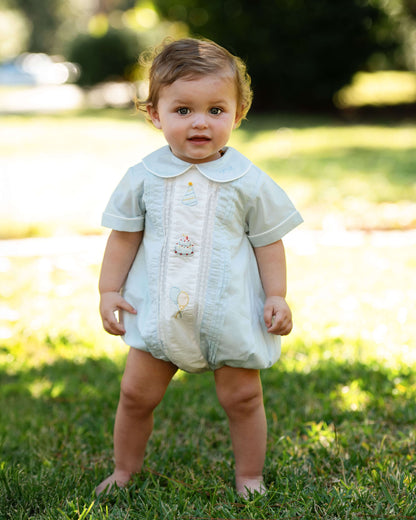 Baby in a light-colored outfit standing on grass