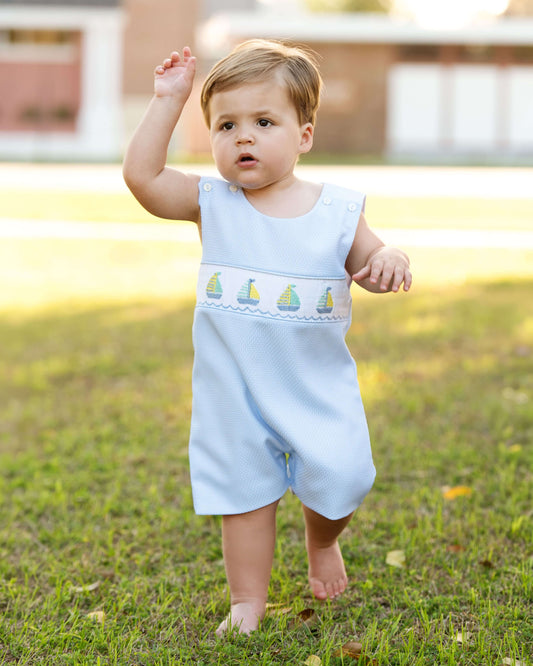 Baby in a light blue dress with sailboat design outdoors on grass