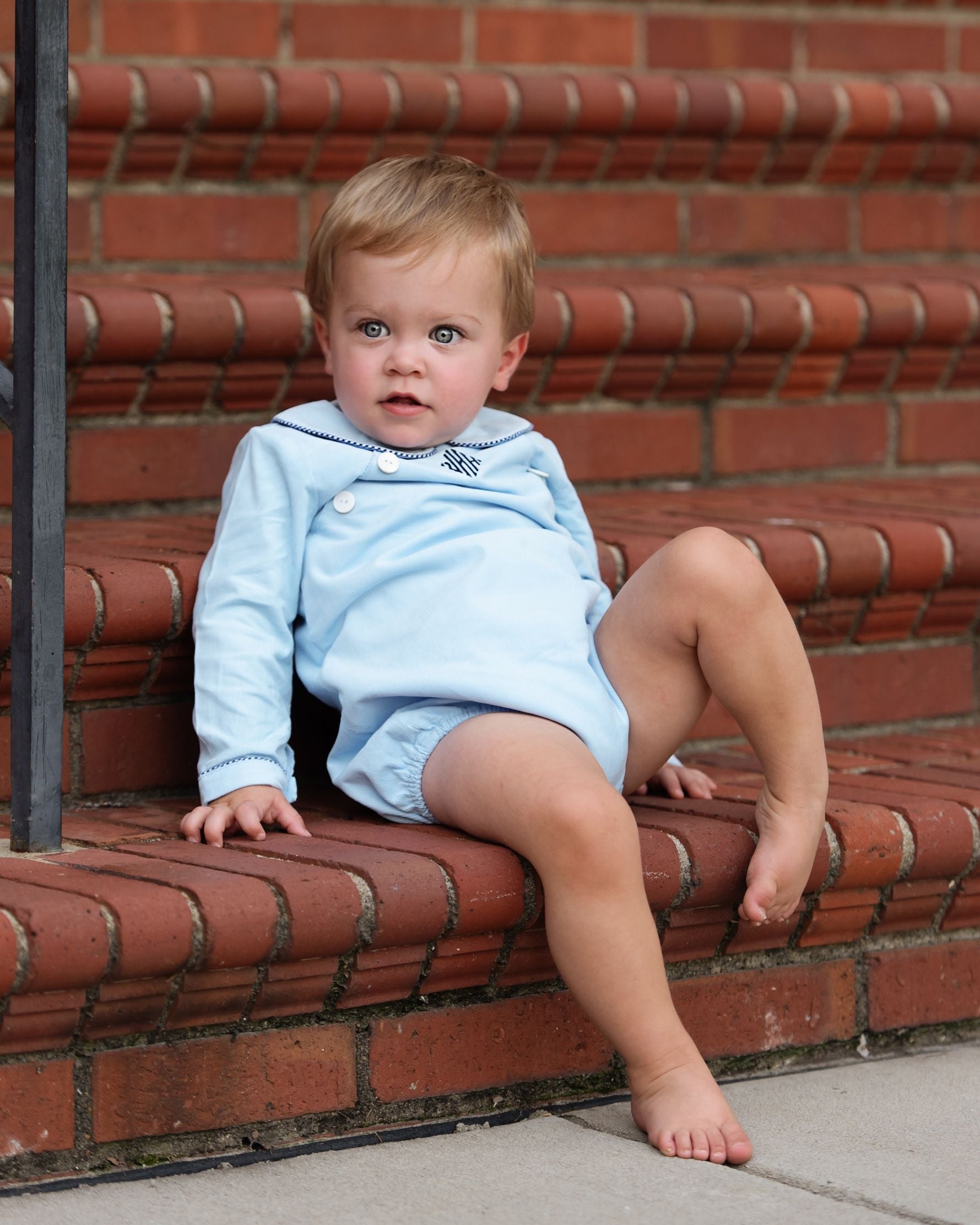 Baby in a light blue outfit sitting on red brick steps.