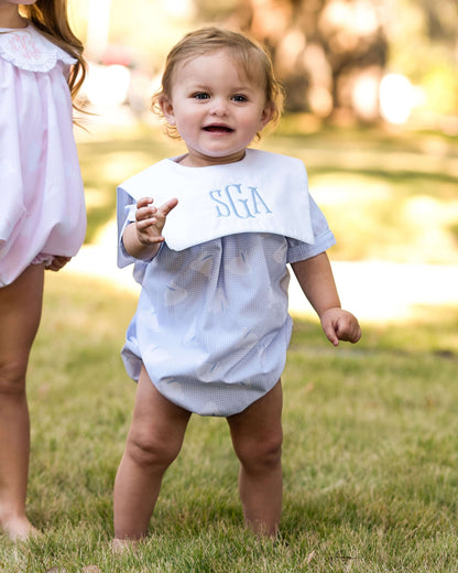 Baby in a light blue outfit with a bib outdoors