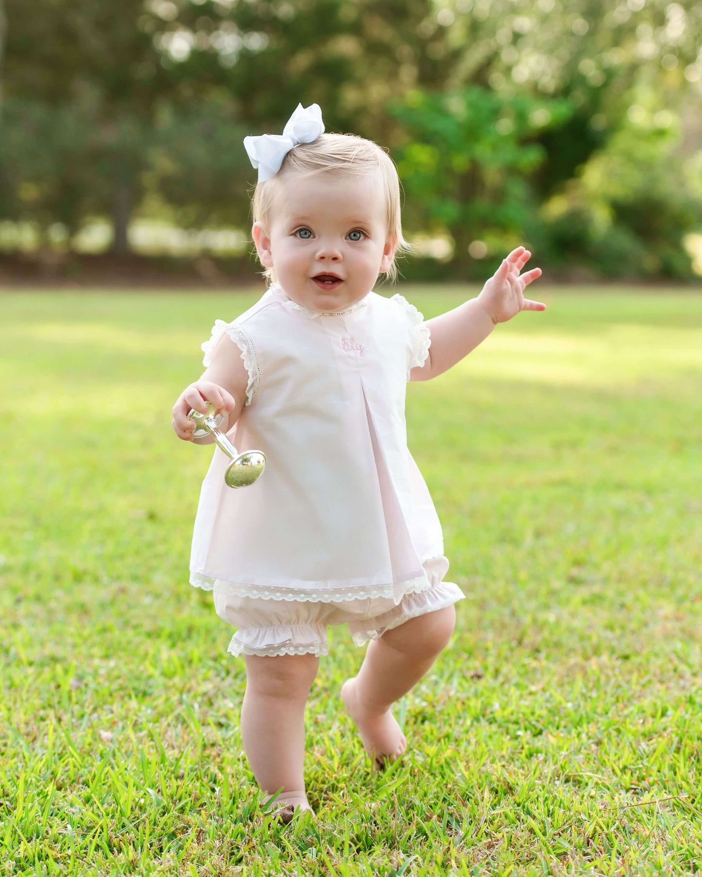 Baby in a pink diaper set with a bow standing on grass