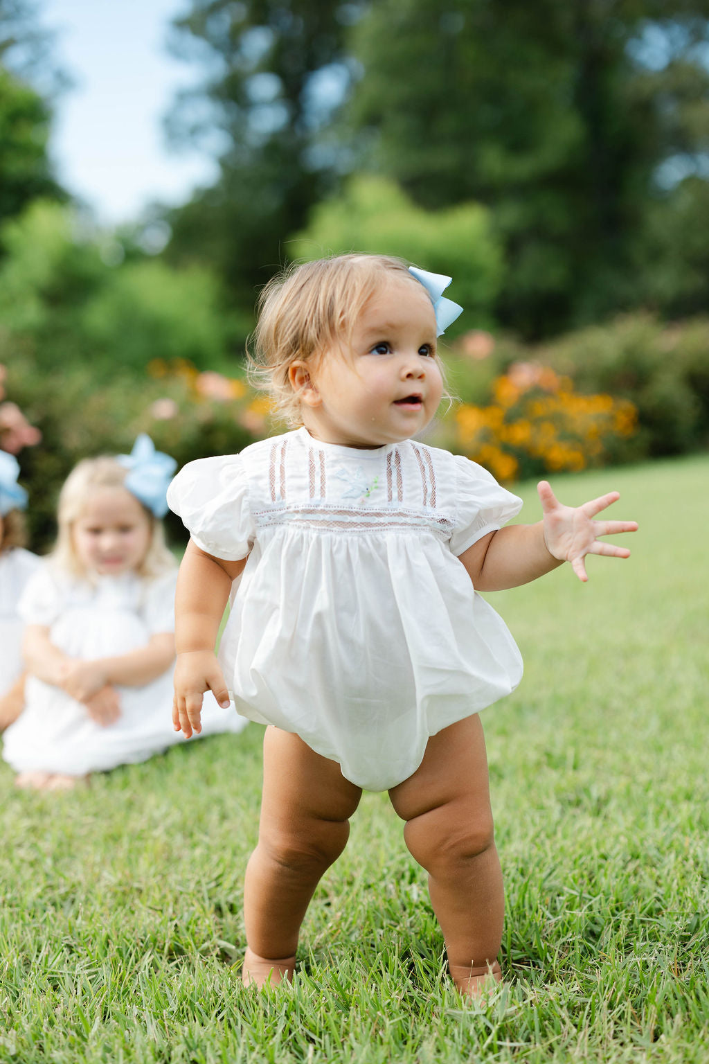 Baby in a white bubble standing on grass with another child in the background