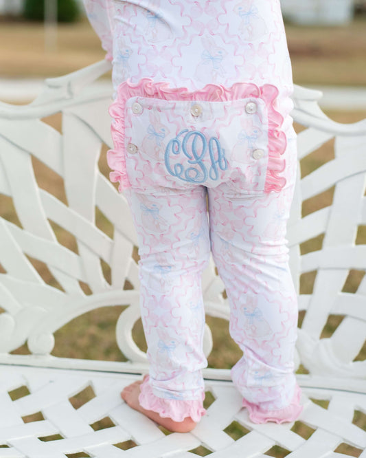 Baby leggings with ruffles and a monogram on a white chair.