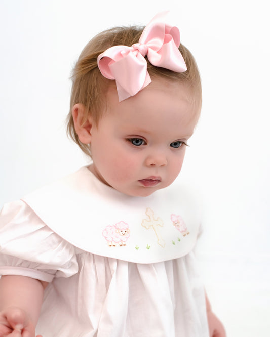 Baby wearing a white dress with a pink bow in her hair on a white background