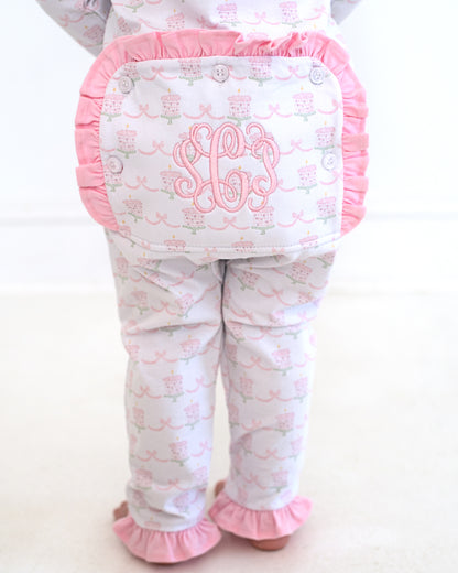 Back view of a toddler wearing pink and white birthday cake print zipper pajamas featuring pink ruffle trim and a monogrammed flap with embroidered initials.