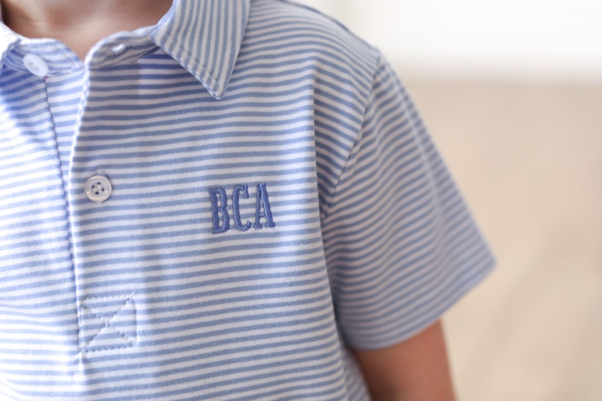 Blue striped shirt with initials BCA on blurred background.