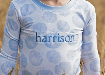 Boy long-sleeve pajama set with blue pumpkin pattern and 'harrison' text on a blurred natural background