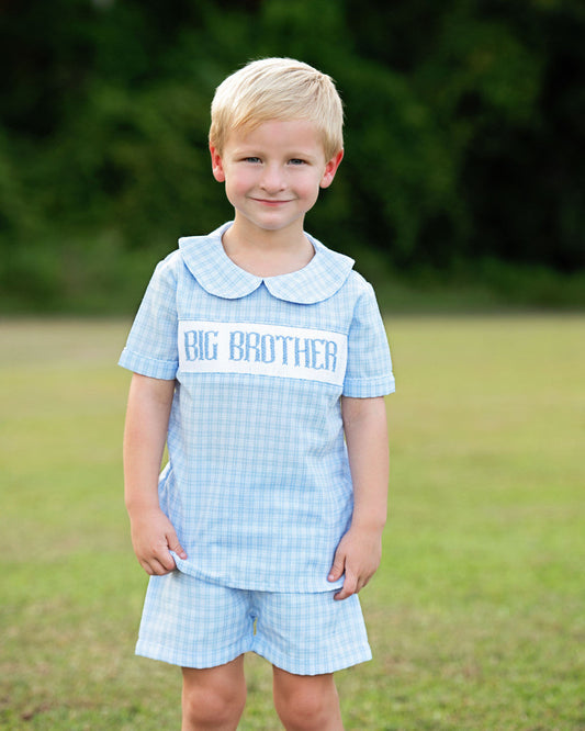 Boy wearing a blue plaid outfit with big brother smocked across the chest.