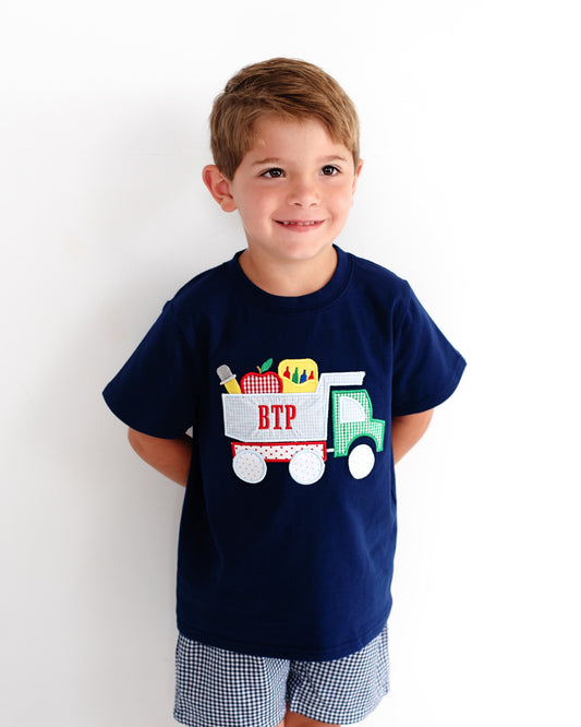 Boy wearing a navy outfit with dump truck and school supplies on the shirt.