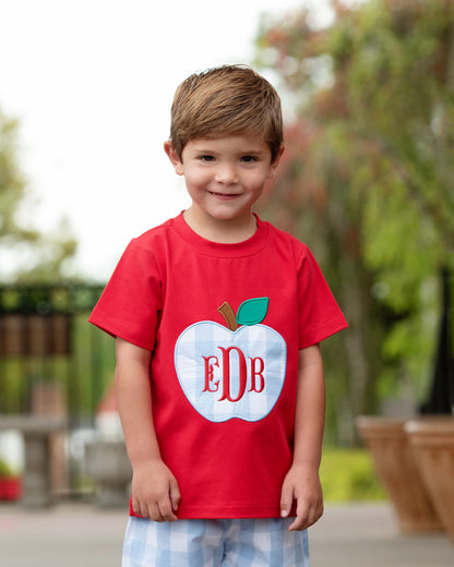 Boy wearing a red shirt with a big apple and blue shorts.