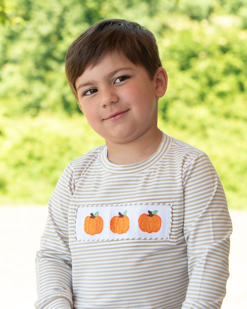 Boy wearing a striped khaki shirt with pumpkin design outdoors