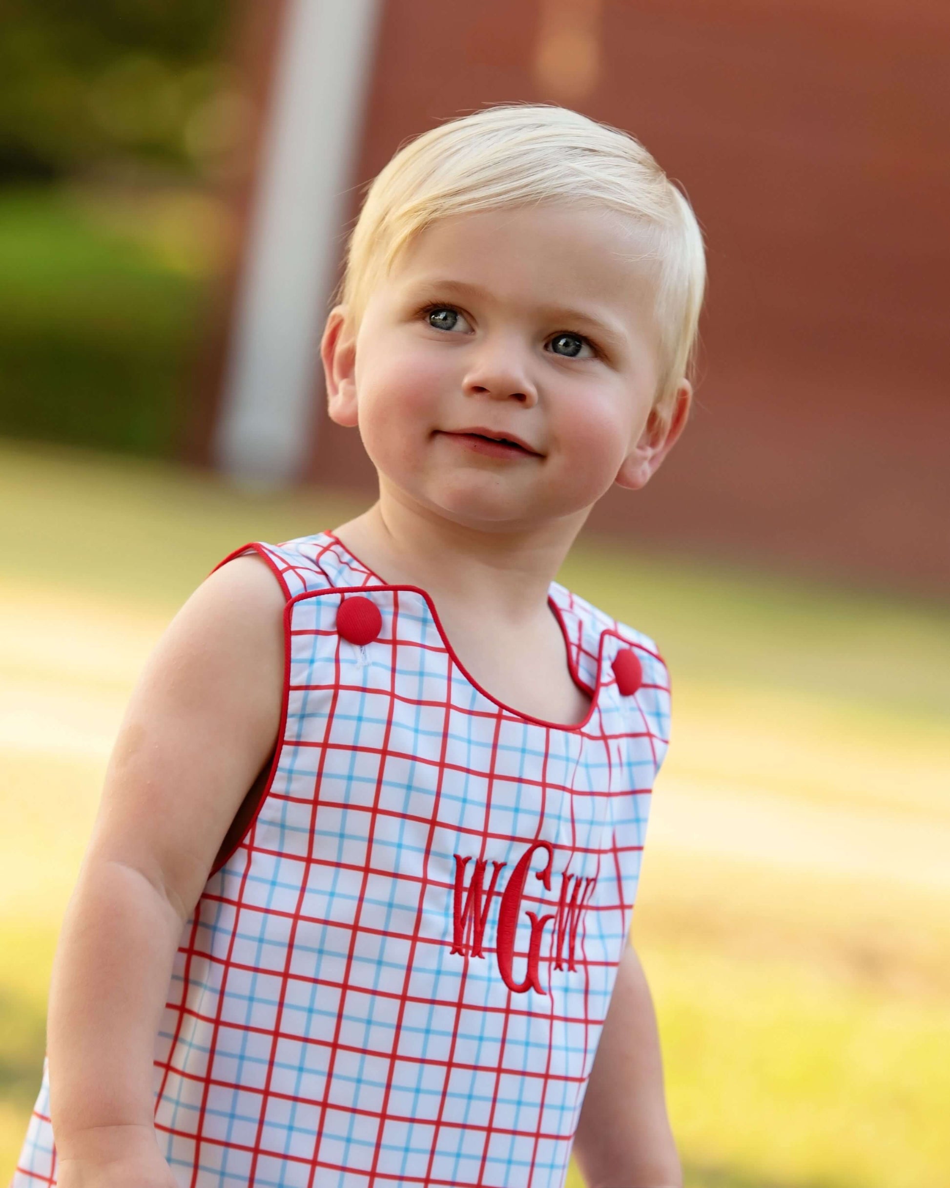 Boy wearing a windowpane outfit with red buttons and a monogram on the chest. 