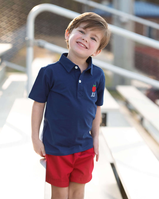 Boy wearing red shorts and a navy polo shirt with an apple 