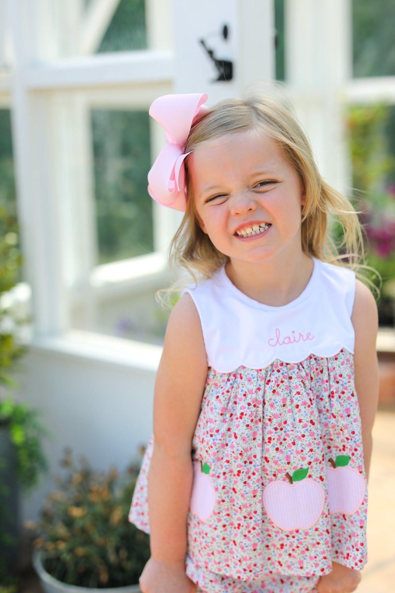 Child cheesing wearing floral top with apples on it