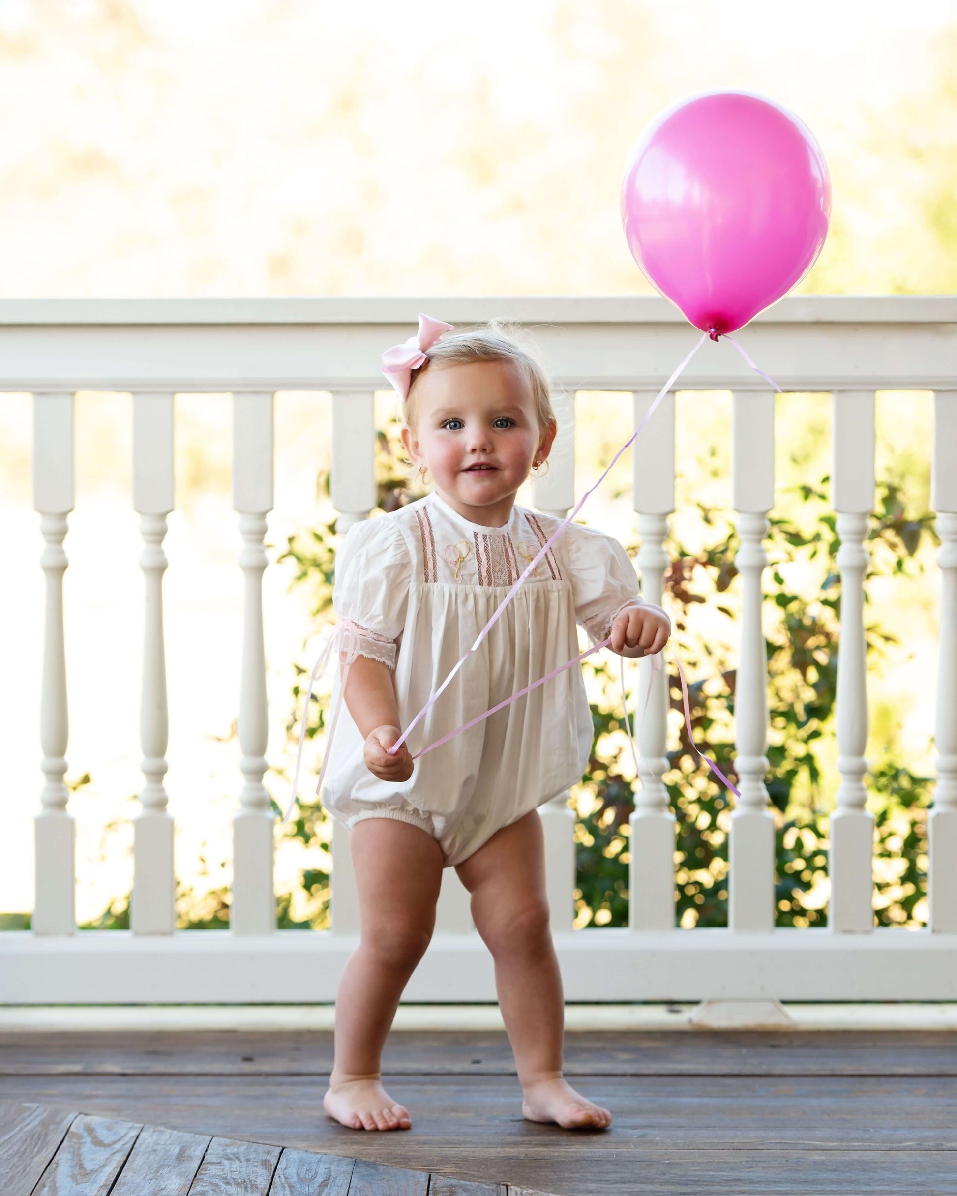 Child holding a pink balloon on a wooden deck with white railings.