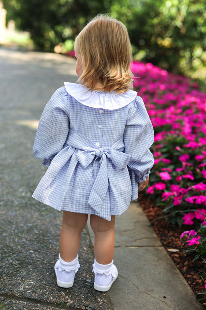 Child in a blue checkered dress standing on a path with pink flowers in the background