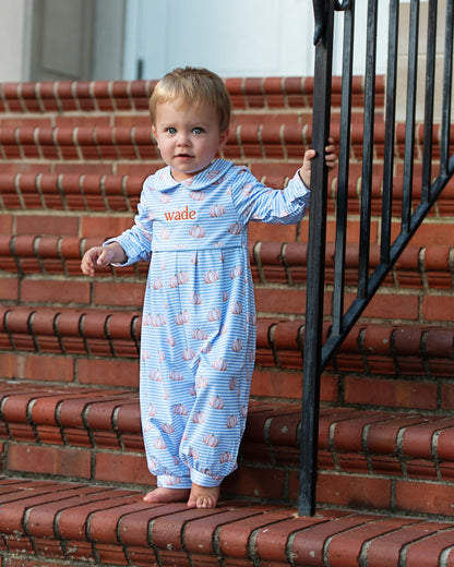 Child in a blue onesie with pumpkin patterns on red brick steps