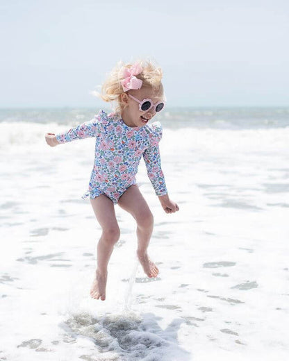 Child in a floral swimsuit playing in the ocean.