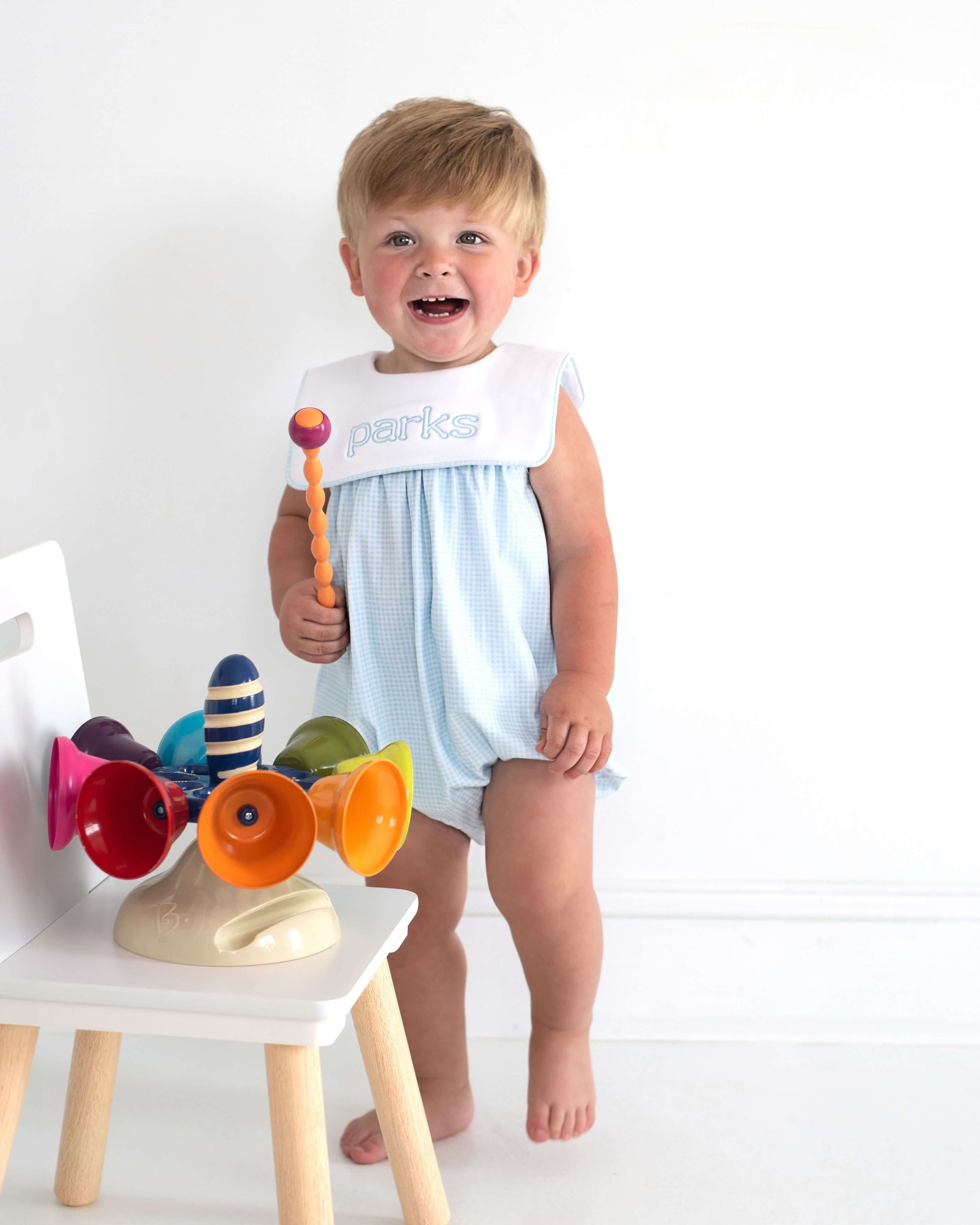Child in a light blue romper with colorful toys on a white background