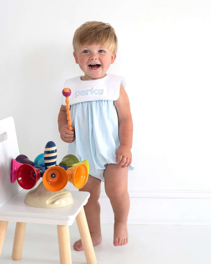 Child in a light blue romper with colorful toys on a white background