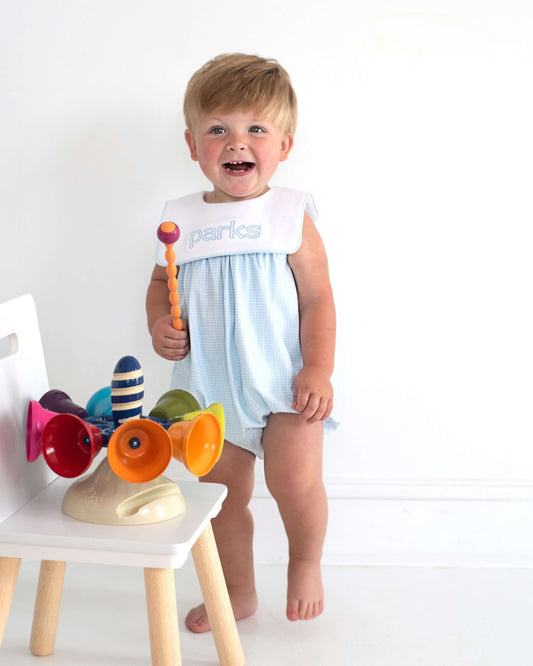 Child in a light blue romper with colorful toys on a white background