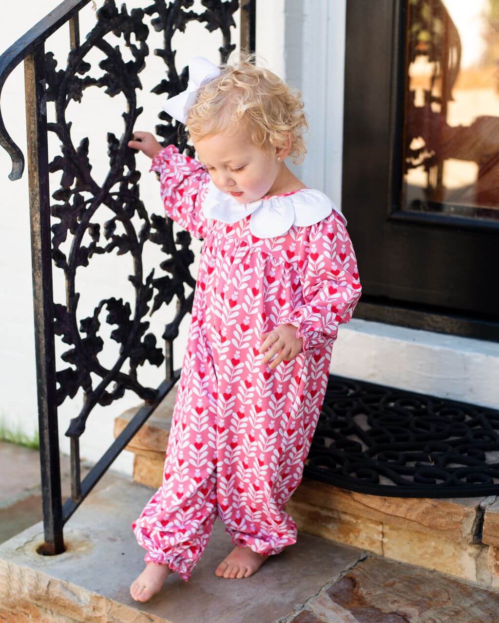 Child in a pink patterned outfit standing on a porch