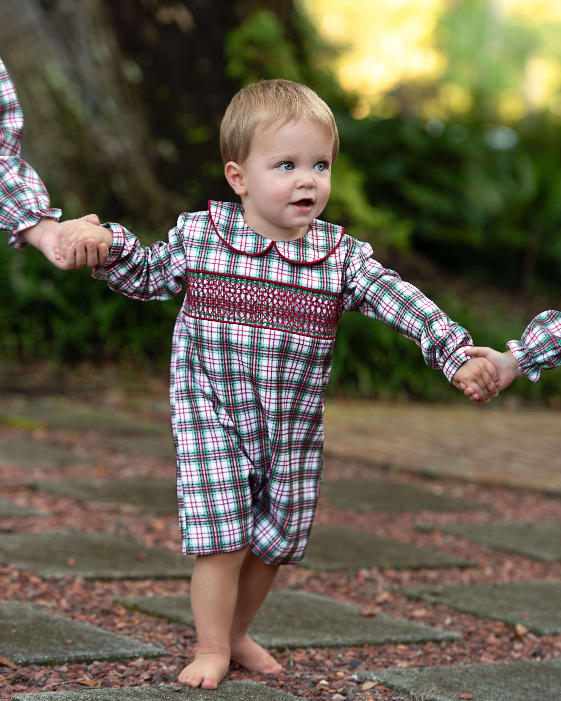 Child in a plaid outfit being held by two adults outdoors.