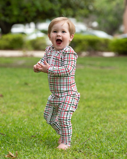 Child in a plaid outfit standing on grass with a blurred background
