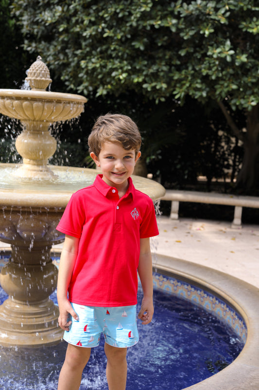 Child in a red polo shirt standing in front of a fountain with greenery in the background