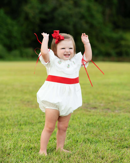 Child in a white dress with red accents standing in a grassy field
