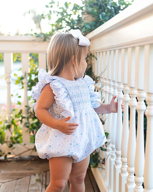 Child in a white smocked floral bubble standing on a porch
