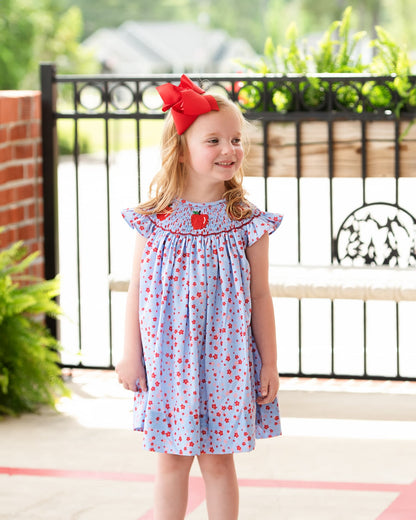 Child in floral dress with smocked apples and a red bow.