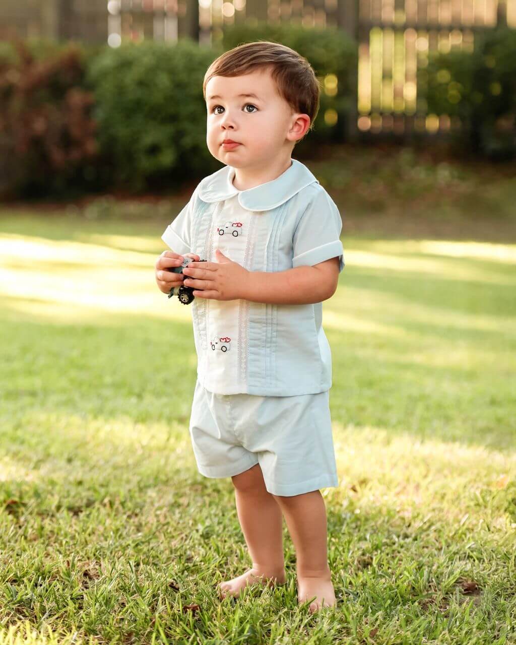 Child in light blue outfit with embroidery, standing on grass