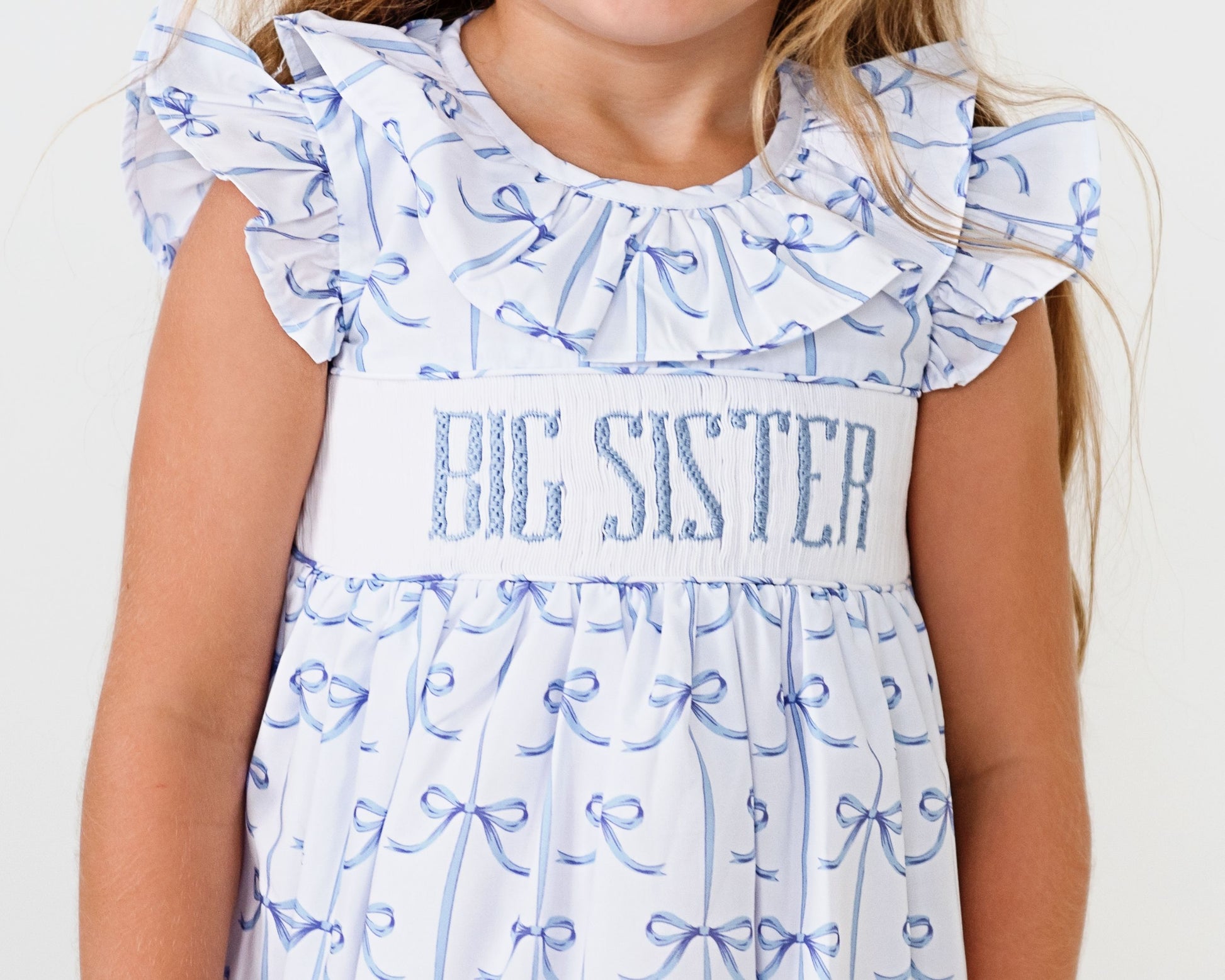 Child wearing a 'BIG SISTER' dress with blue ribbon patterns on a white background