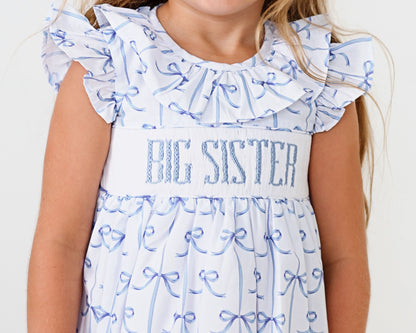Child wearing a 'BIG SISTER' dress with blue ribbon patterns on a white background