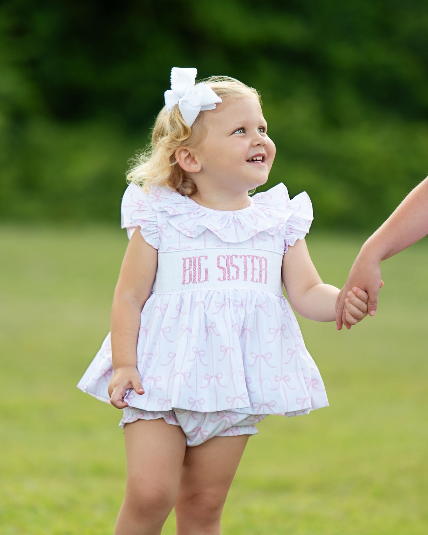 Child wearing a 'Big Sister' outfit outdoors on a grassy background