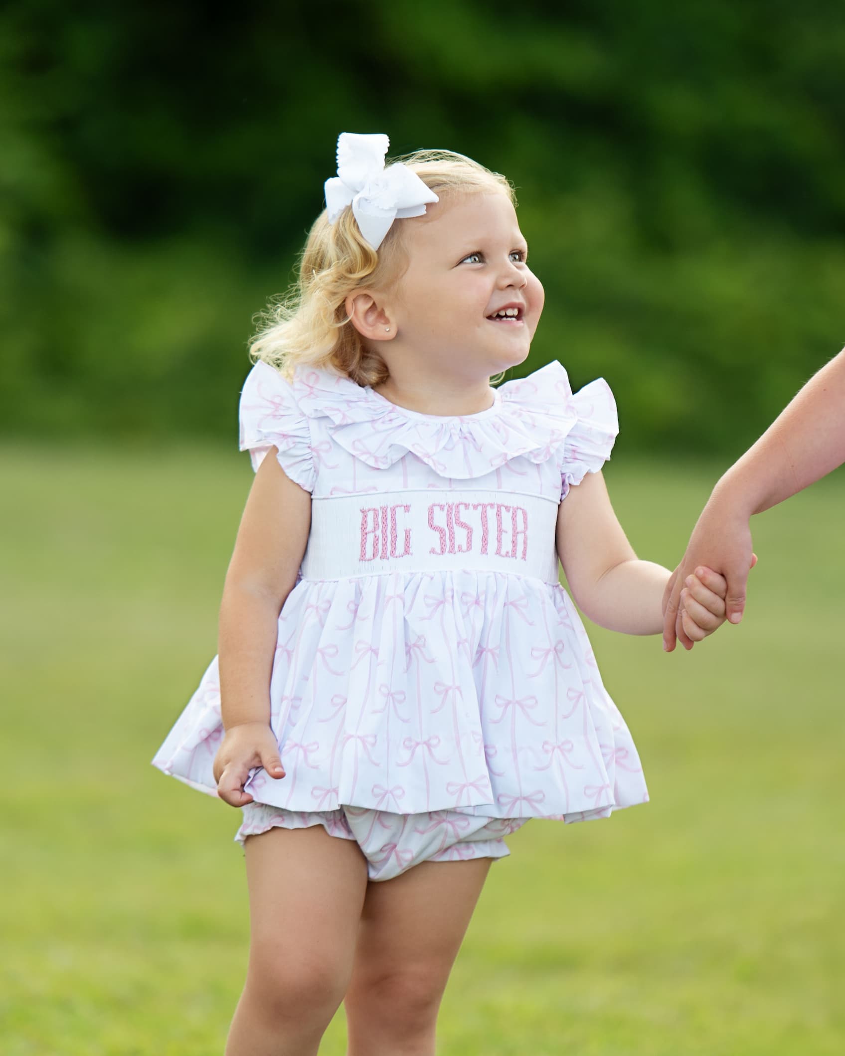 Child wearing a 'Big Sister' outfit outdoors on a grassy background
