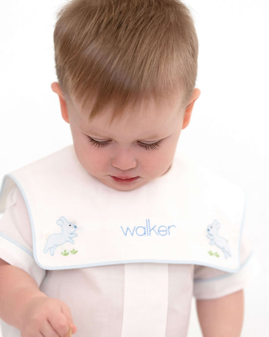 Child wearing a bib with embroidered designs and text on a white background