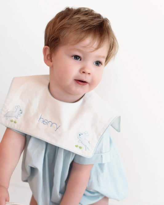 Child wearing a bib with embroidered name and designs on a plain background