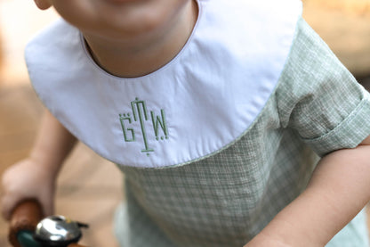 Child wearing a bib with initials 'GTV' in a green font.