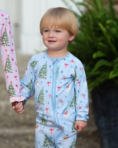 Child wearing a blue Christmas-themed pajama with pink sleeves featuring tree designs.