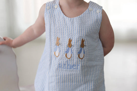 Child wearing a blue and white striped bubble with embroidered bunnies and name.
