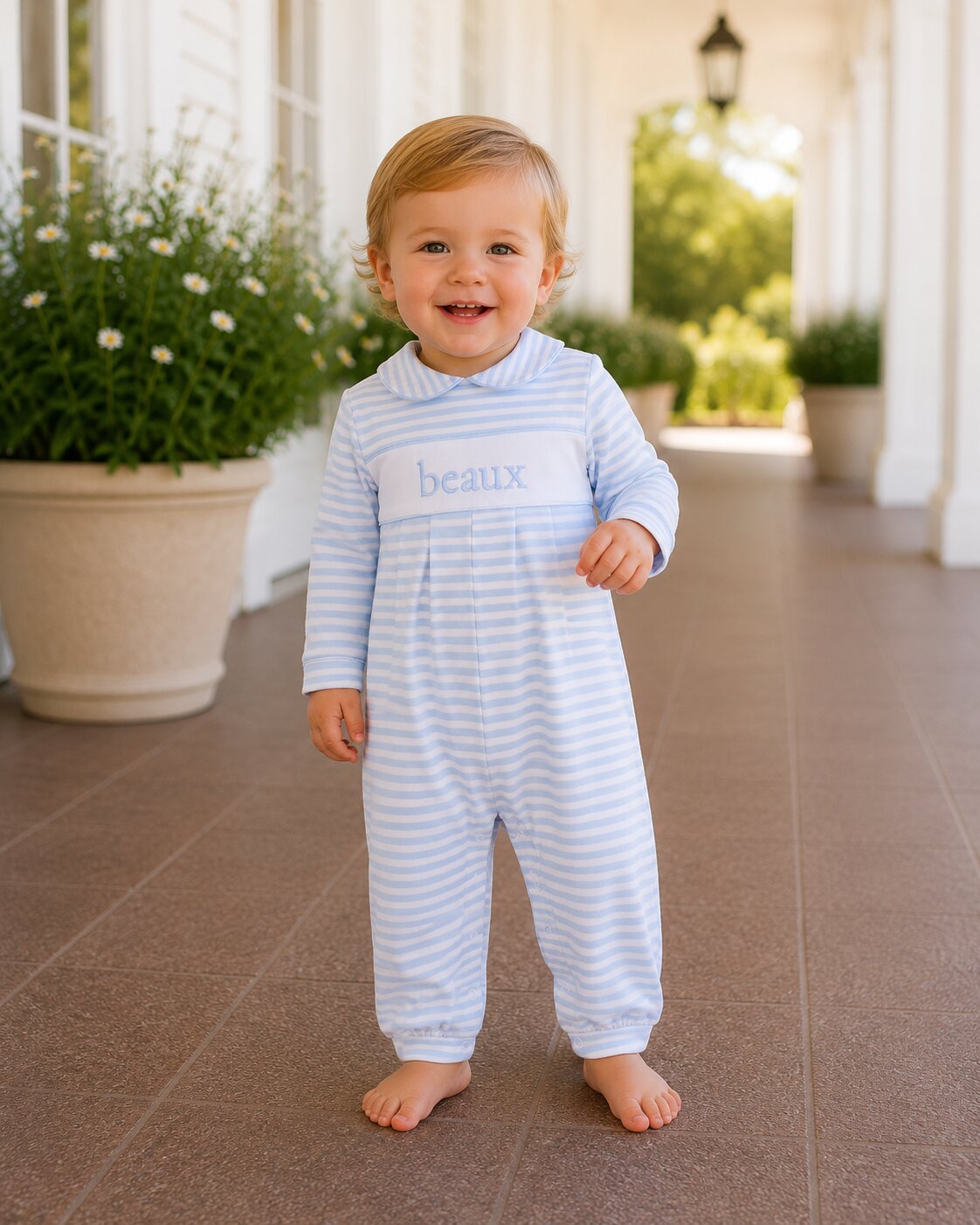 Child wearing a blue and white striped outfit with 'beaux' print, standing on a patio.