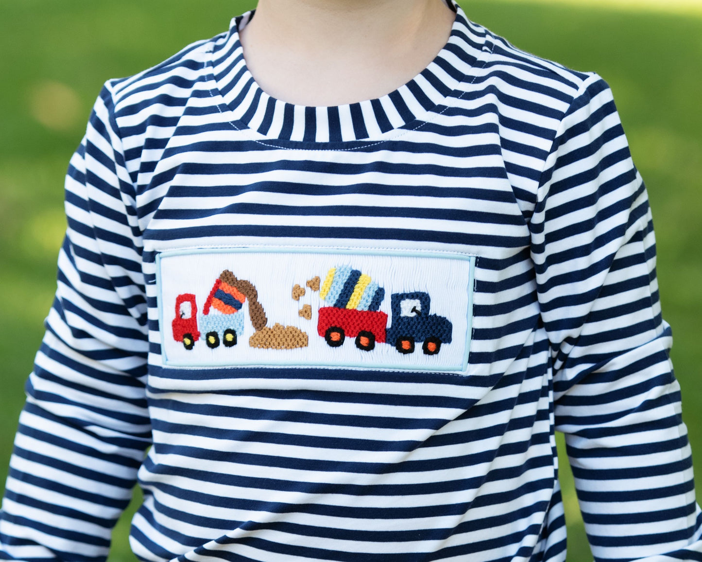 Child wearing a blue and white striped shirt with a construction-themed pocket design.
