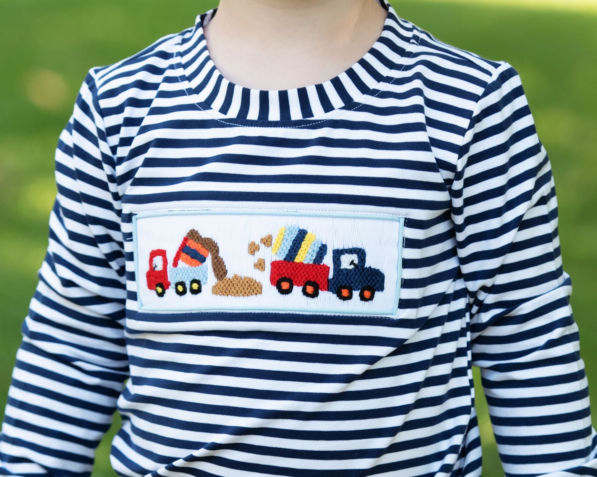 Child wearing a blue and white striped shirt with a construction-themed pocket design.